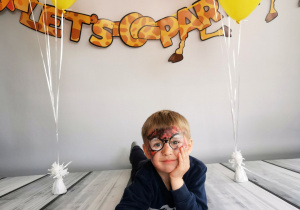 Chłopiec leży na tle fotograficznym i pozuje do zdjęcia wśród balonów.